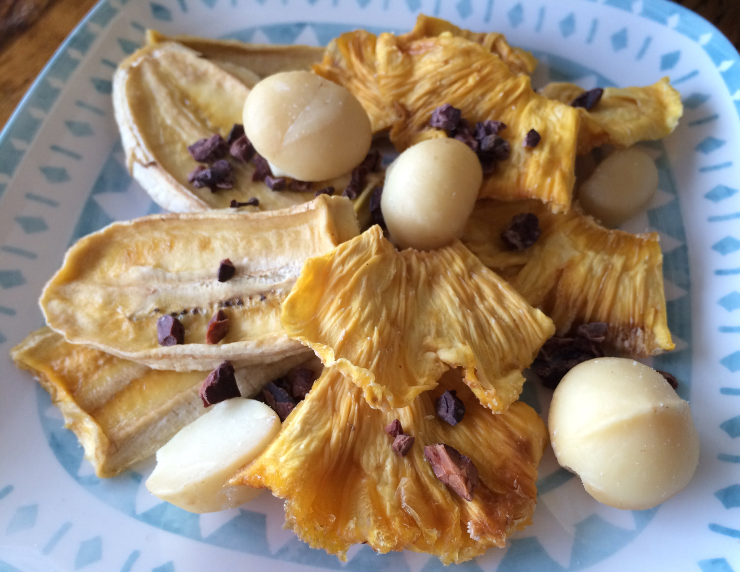 A small plate of dehydrated yellow Hawaiʻian Sweet Gold brand pineapple, apple bananas, cacao nibs, and macadamia nuts.